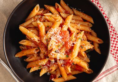 A bowl of penne pasta topped with tomato sauce and grated cheese
