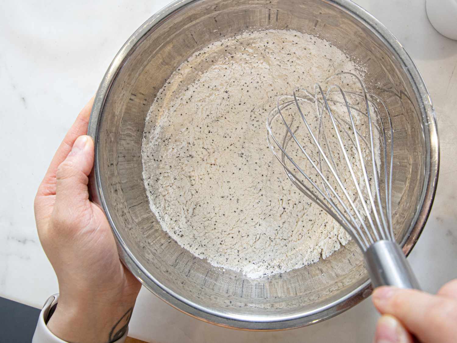 Person mixing dry ingredients in a bowl with a whisk