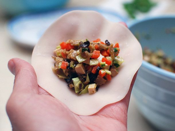 Hand holding a round dumpling wrapper with vegetable filling in the center.