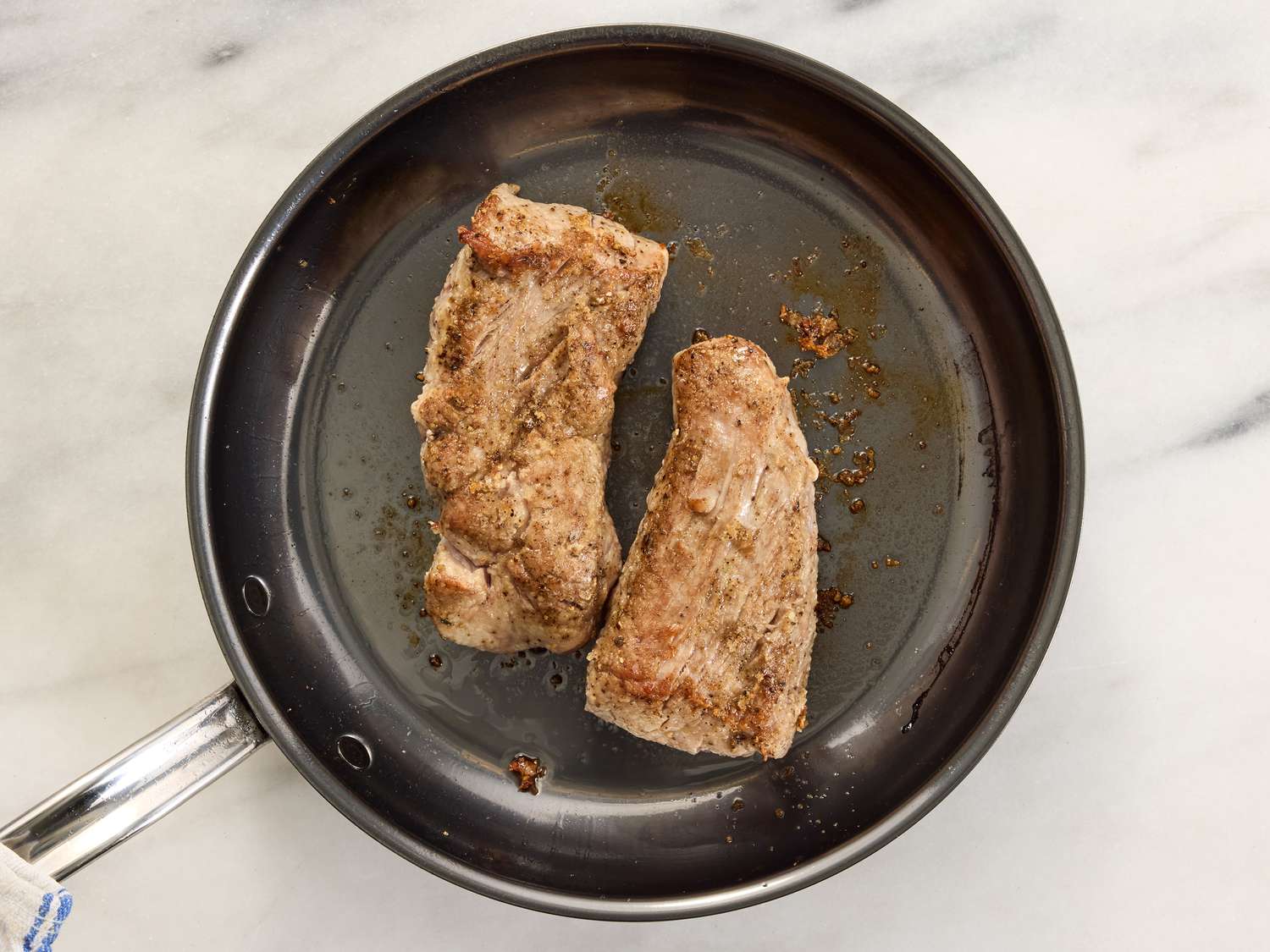 Pork browning in a skillet on a white marble surface 