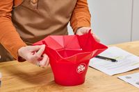 A person holds the Chef'n Pop Top Microwave Popcorn Maker by the sides