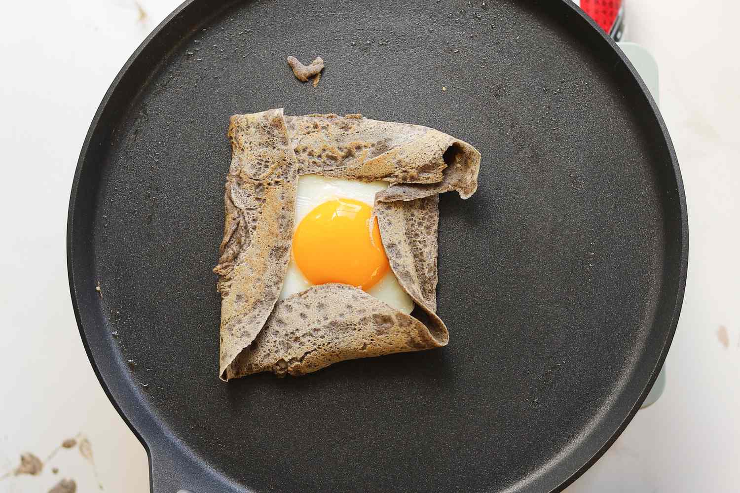 A buckwheat crepe with a fried egg in the middle on a crepe pan.