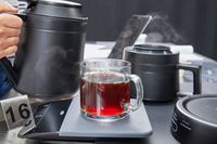 Coffee in a mug on a scale next to a hand holding the Ratio Six Coffee Maker's carafe.
