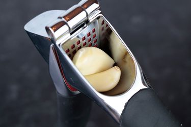 the hopper of a garlic press with two cloves inside of it