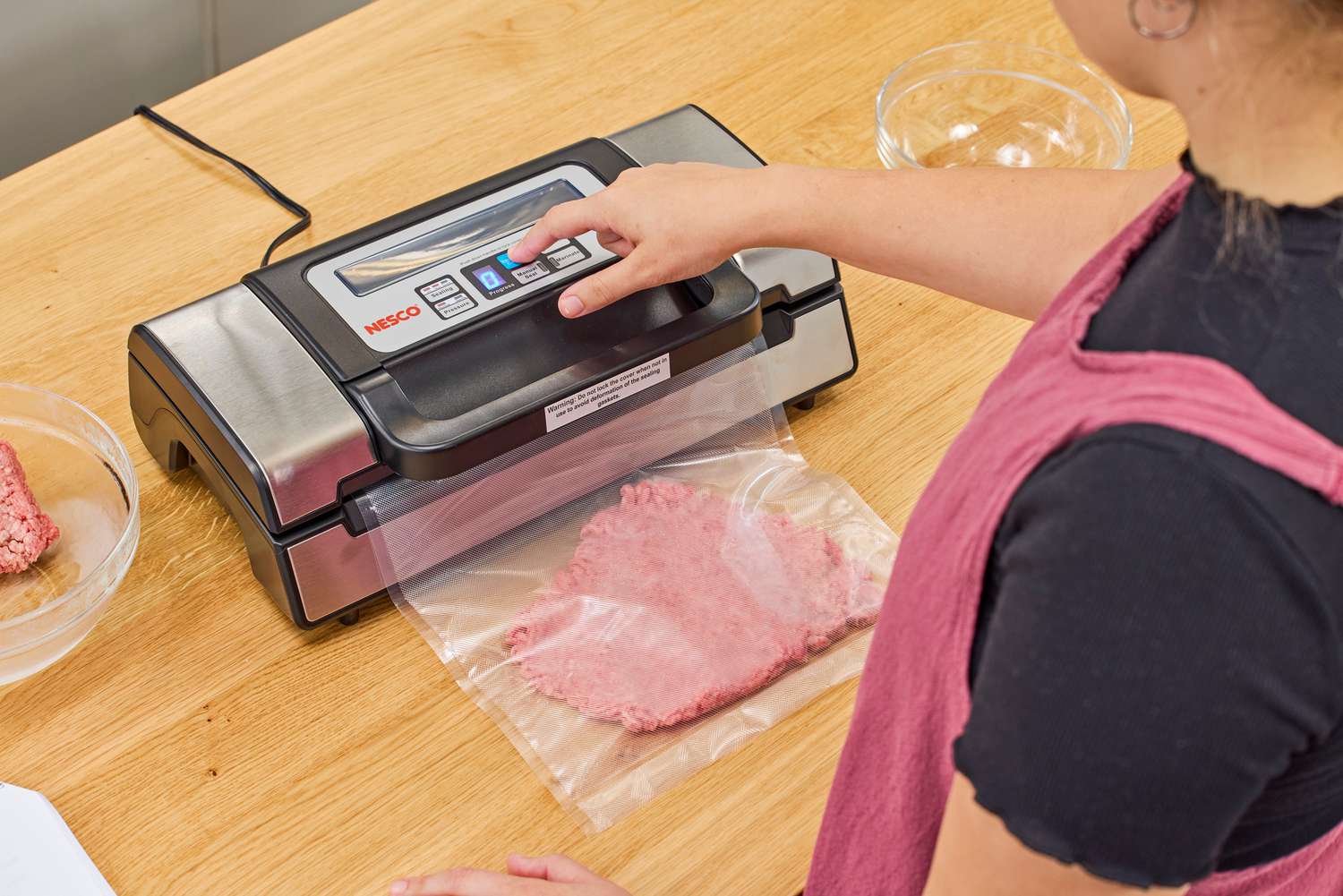 A person vacuum seals a bag of meat using the Nesco VS-12 Deluxe Vacuum Sealer