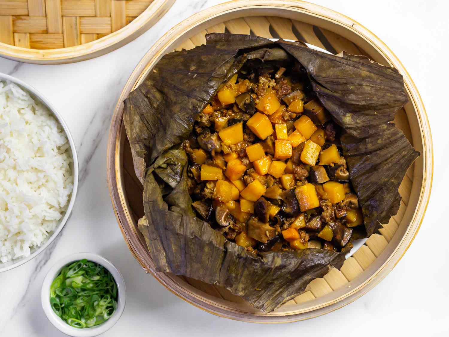 Overhead view of leaf-wrapped winter squash with pork and shiitakes, partially unwrapped and served in a bamboo steamer insert.