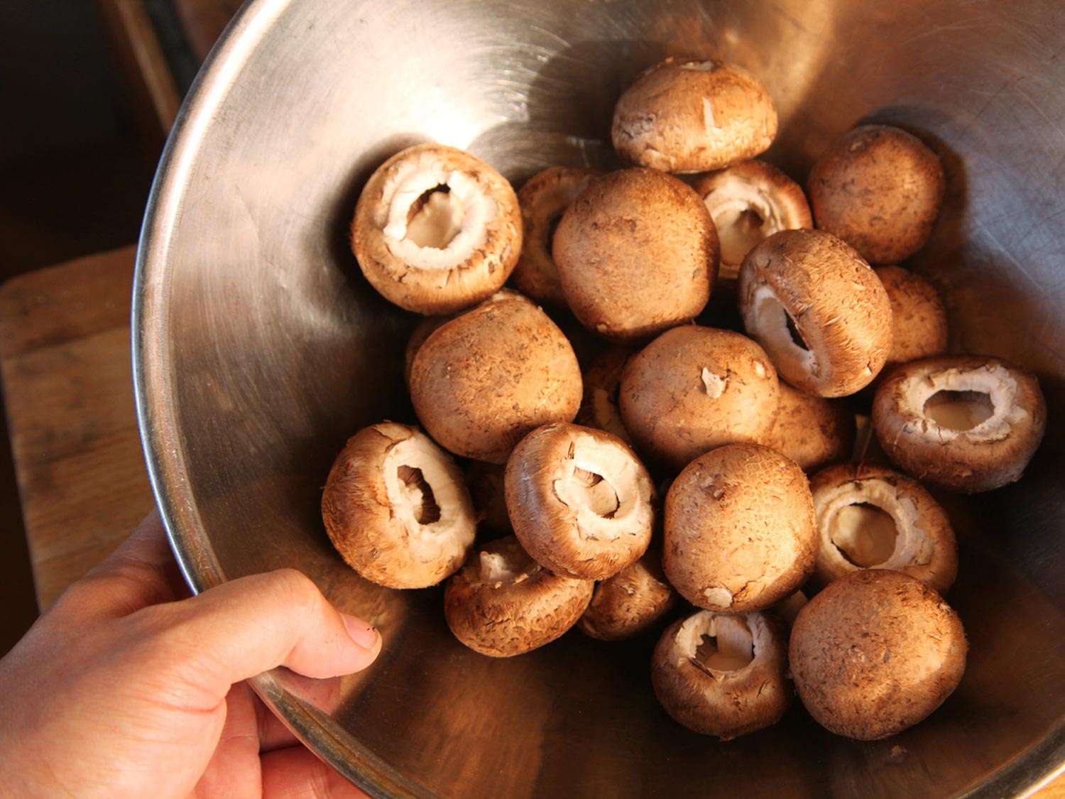 A bowl of stemmed mushrooms being held by a hand.