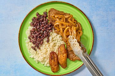 Onions placed on top of steaks, with sides of rice, plantains and beans 
