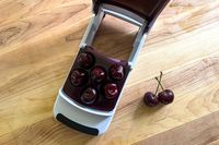 An overhead view of the OXO Good Grips Multi Cherry Pitter with two cherries next to it.