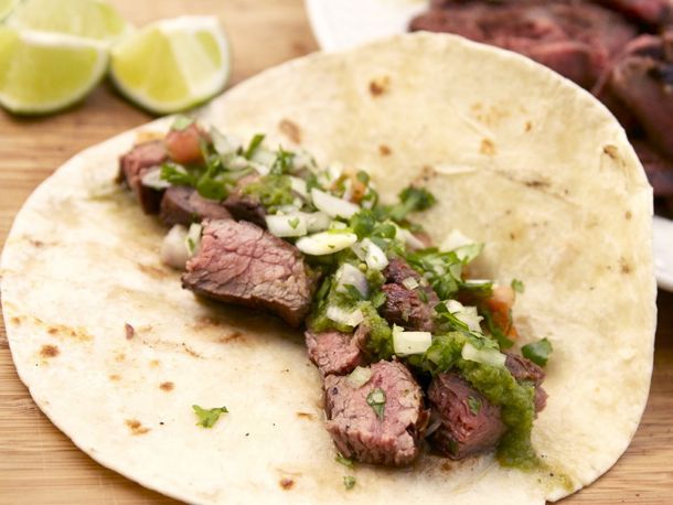 Sliced marinated grilled flank steak nestled in a flour tortilla and topped with green salsa. 