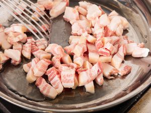 Diced pancetta in a skillet being stirred with a slotted spatula