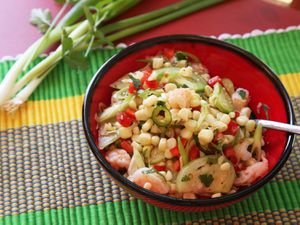 Shrimp, corn, and tomatillo salad, served in a red bowl on a colorful placemat.