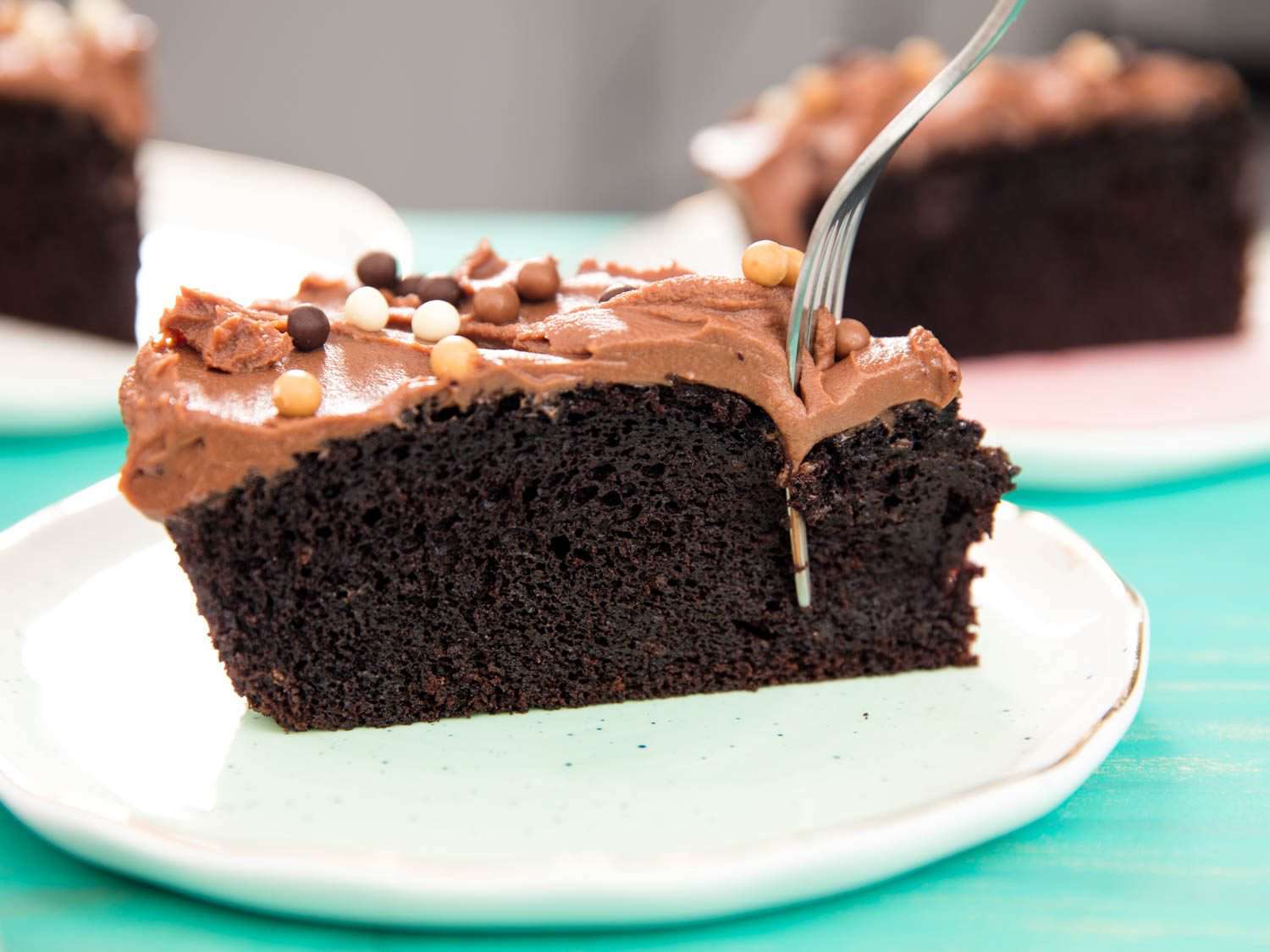 A fork piercing through a slice of chocolate cake with milk-chocolate ganache frosting.