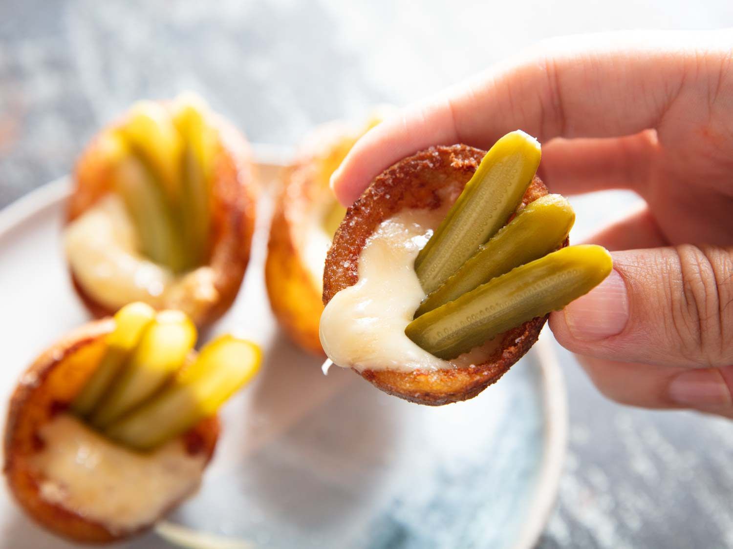 Deep-fried potato skin cups filled with melted raclette cheese ad thinly sliced gherkins.