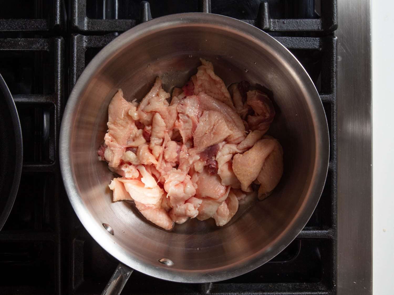 Overhead of pieces of raw duck fat and skin in a saucepan.