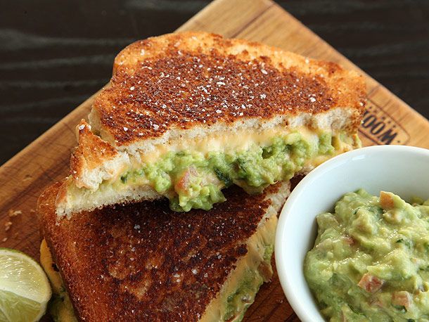 Grilled cheese with guacamole sandwich cut into halves and served with extra guacamole.