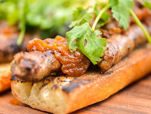 Grilled mergez on grilled baguette with caramelized onions, Manchego cheese, and a few sprigs of cilantro