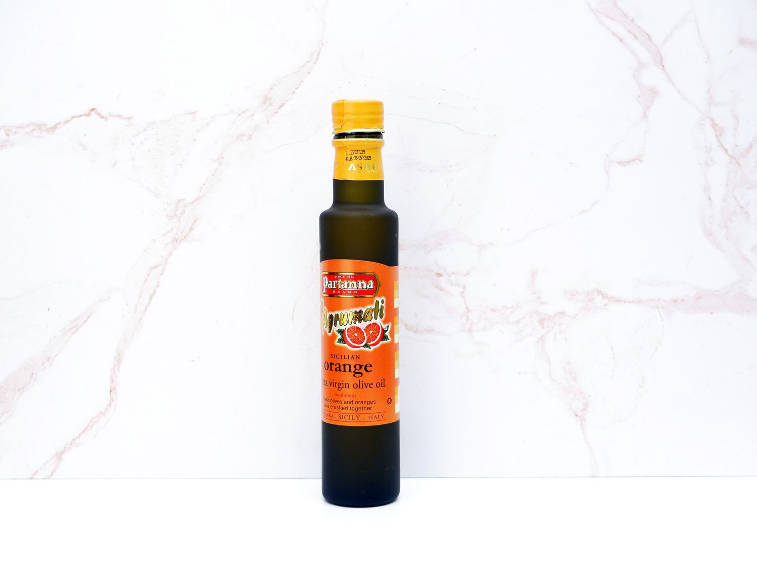 Partanna Sicilian orange olive oil on a pale pink marble backdrop