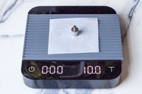A small weight placed on a piece of paper atop a Acaia Pearl scale displaying 10.0