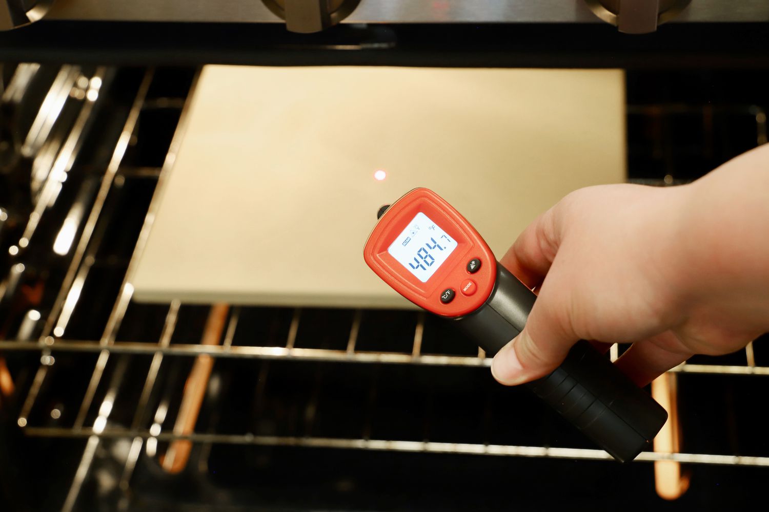 An infrared thermometer being used to take the temperature of a pizza stone in an oven.