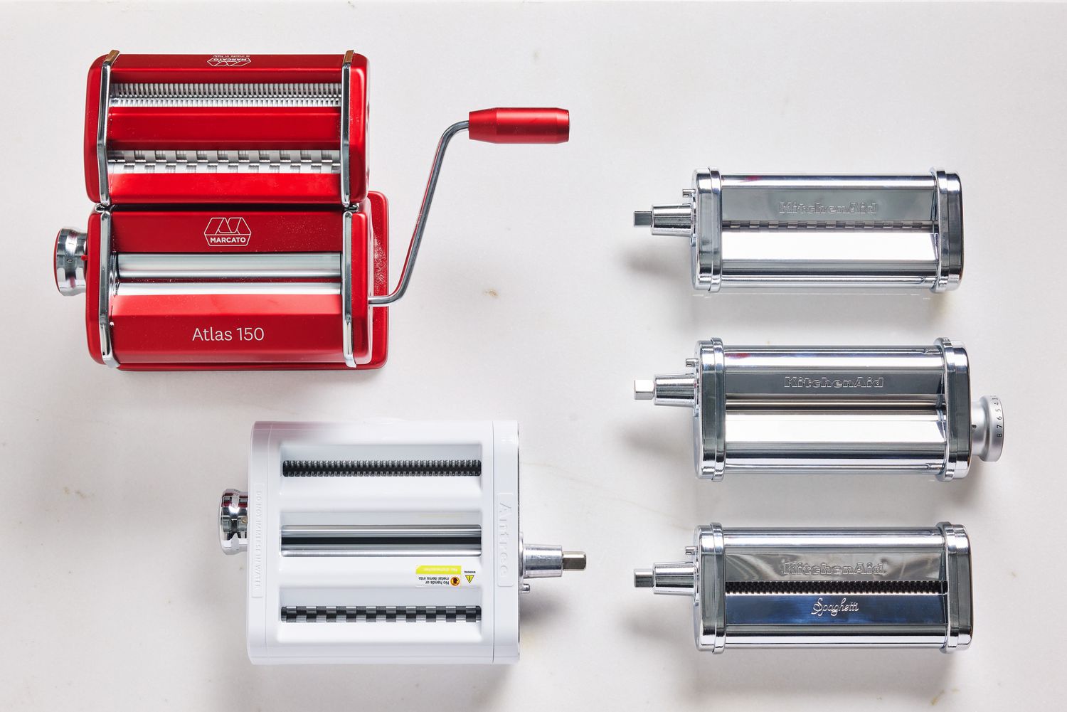 Three manual pasta makers on a white kitchen countertop