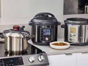 Three pressure cookers sitting on a kitchen counter with a bowl of cooked food in front of them