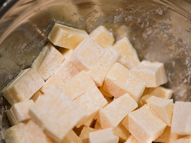 Cubes of cheese are tossed with cornstarch in a mixing bowl.