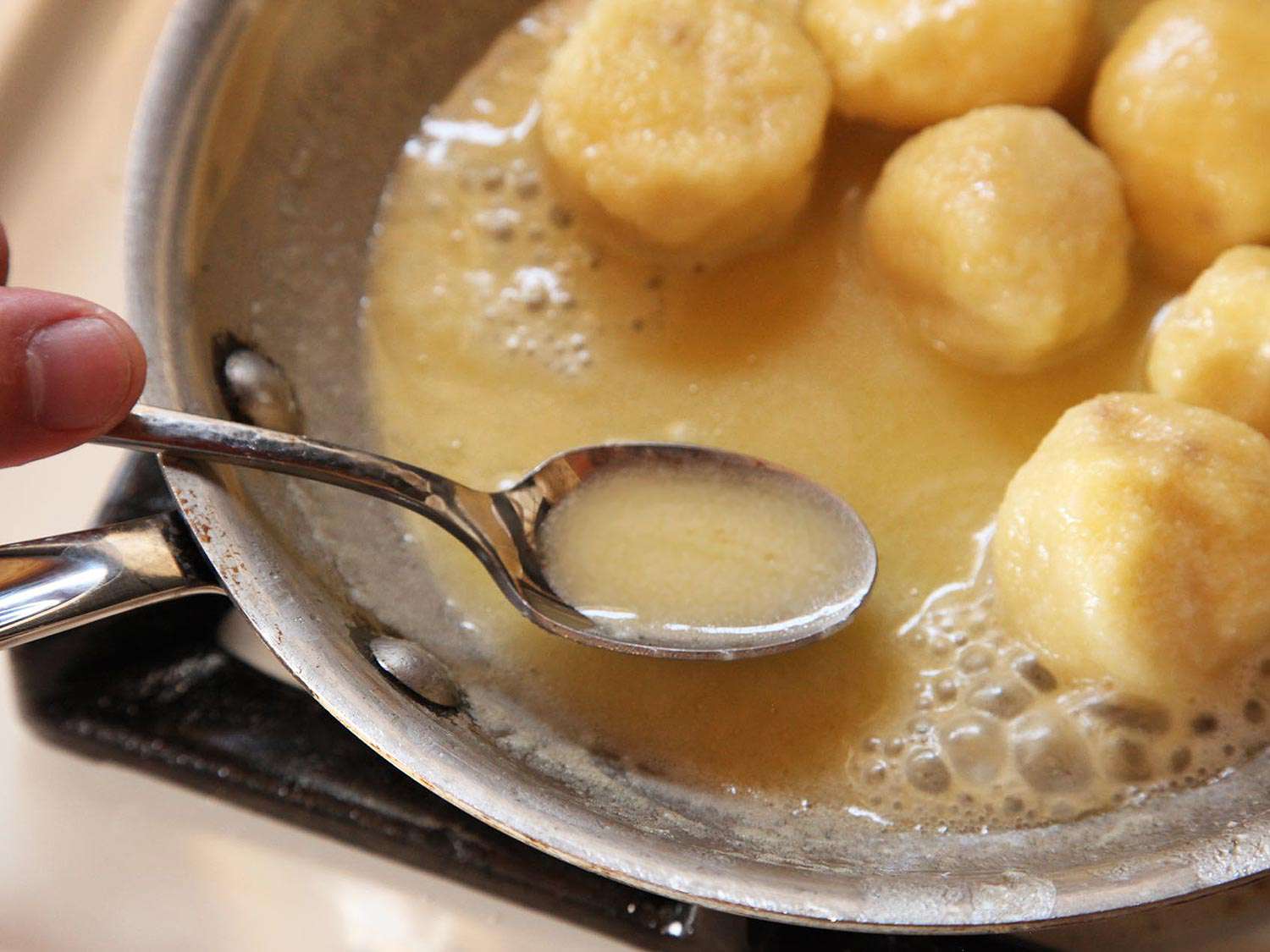 A spoonful of sauce from a skillet cooking gnudi. 