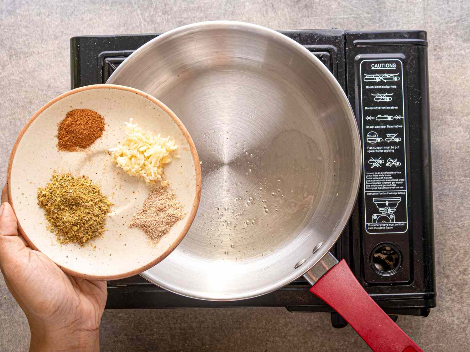 A plate with spices and minced garlic held over a pan on a stovetop