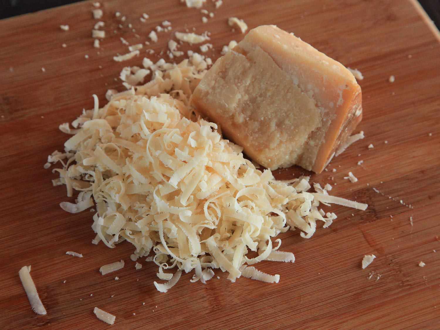 Grated Parmigiano Reggiano piled next to a chunk of the cheese on a cutting board.