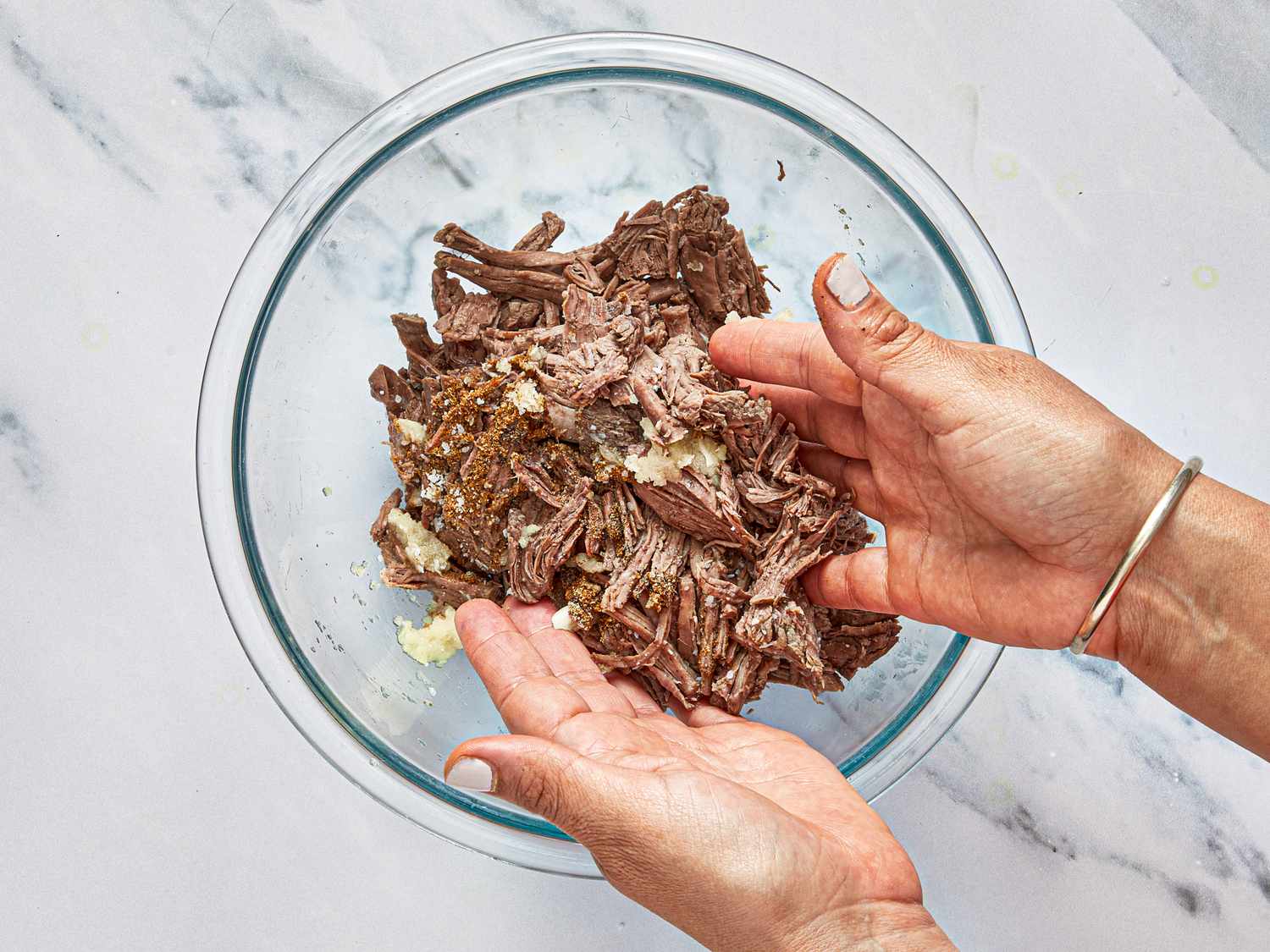 Hands mixing shredded beef in a glass bowl for preparation