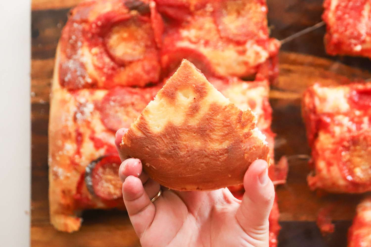 A person holding a pizza made in the LloydPans 12x12x1.5 inch Sicilian Style Pizza Pan