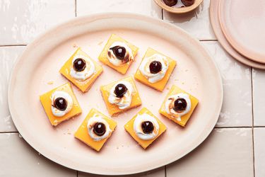 Amaretto Lemon Bars on a warm blush colored plate and tile surface. smaller serving plates and a small bowl of cherries to the side