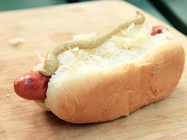 A grilled hot dog in a bun topped with sauerkraut and mustard