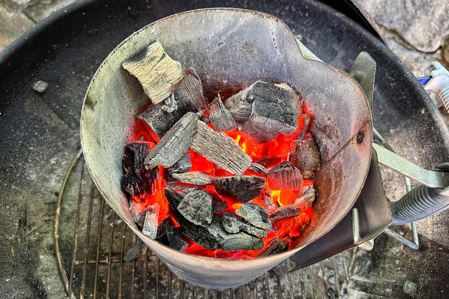 Charcoal briquettes glowing with heat in a metal chimney starter used for grilling