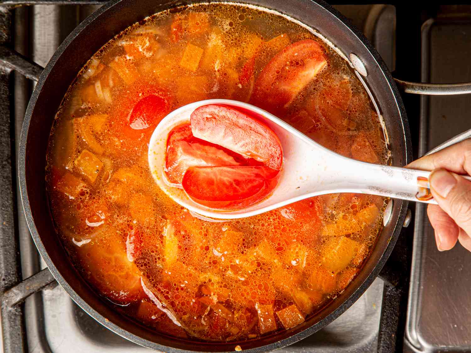 Overhead view of whole tomatoes being added to fish broth