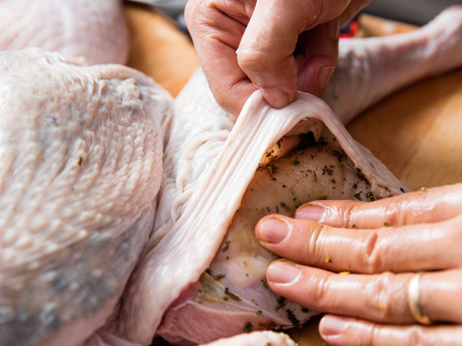 Closeup of author slipping herb-garlic paste under the skin of a turkey leg quarter.