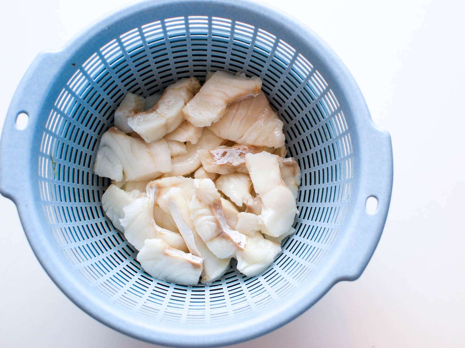 Overhead view of velveted chicken slices draining in a plastic colander.