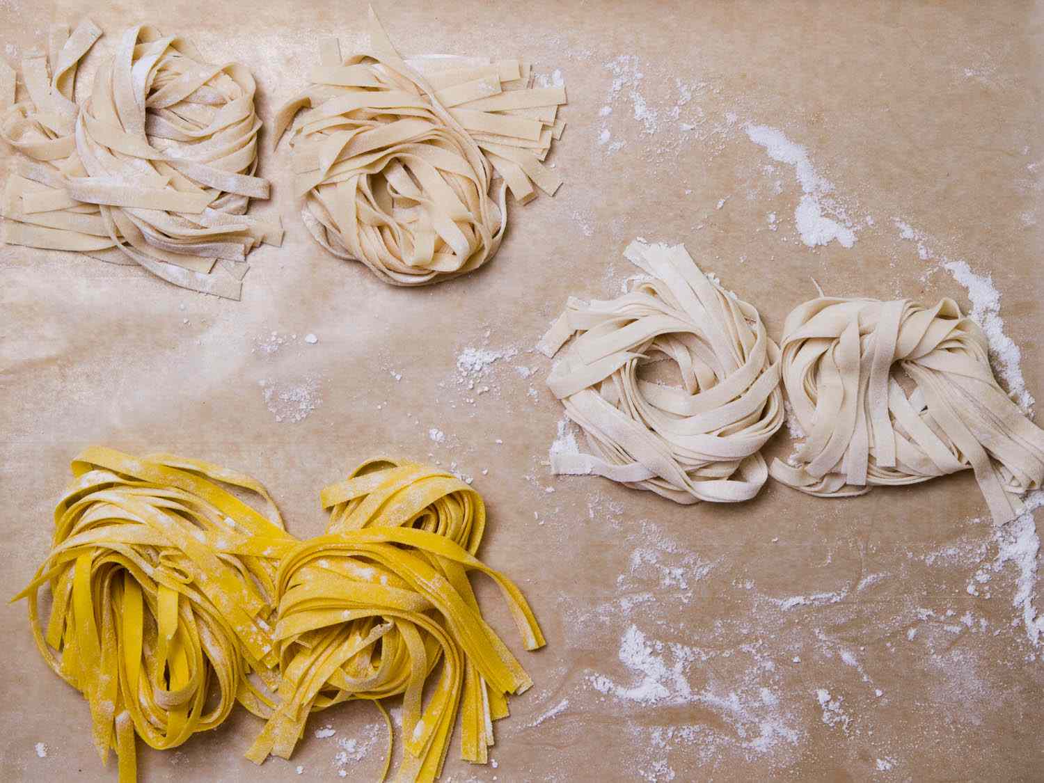 Clusters of different types of fresh pasta strands in three colors: yellow, beige, and white. 