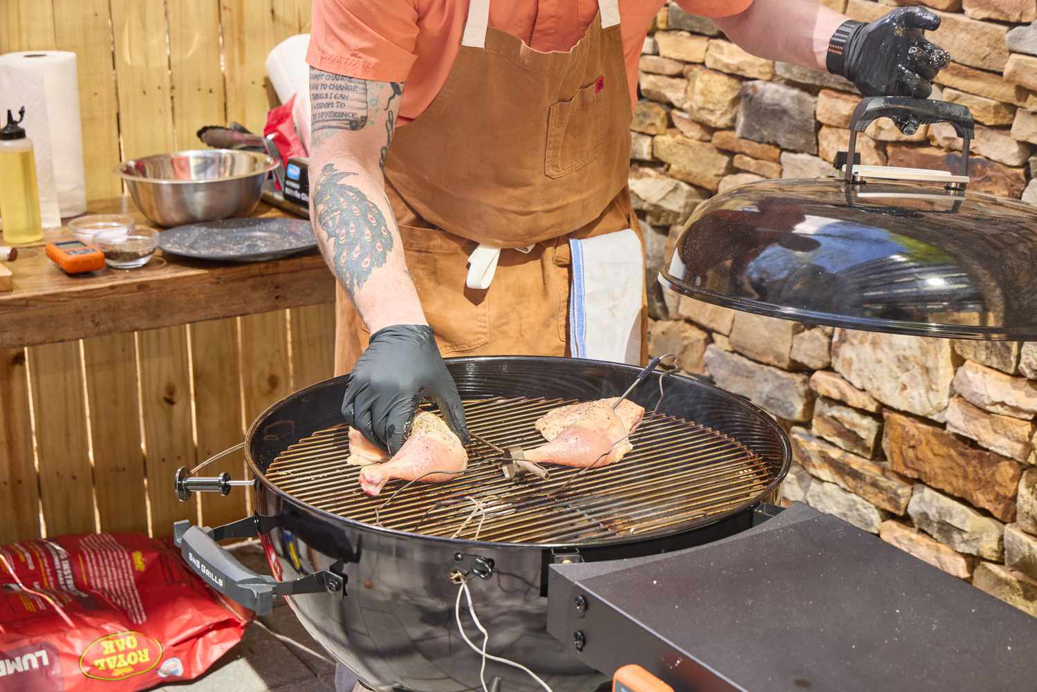 A person placing raw chicken into the SNS Grills Slow 'N Sear Original 22-Inch Kettle Grill