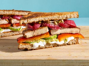 A marinated tofu sandwich layered with vegetables and spread on whole grain bread