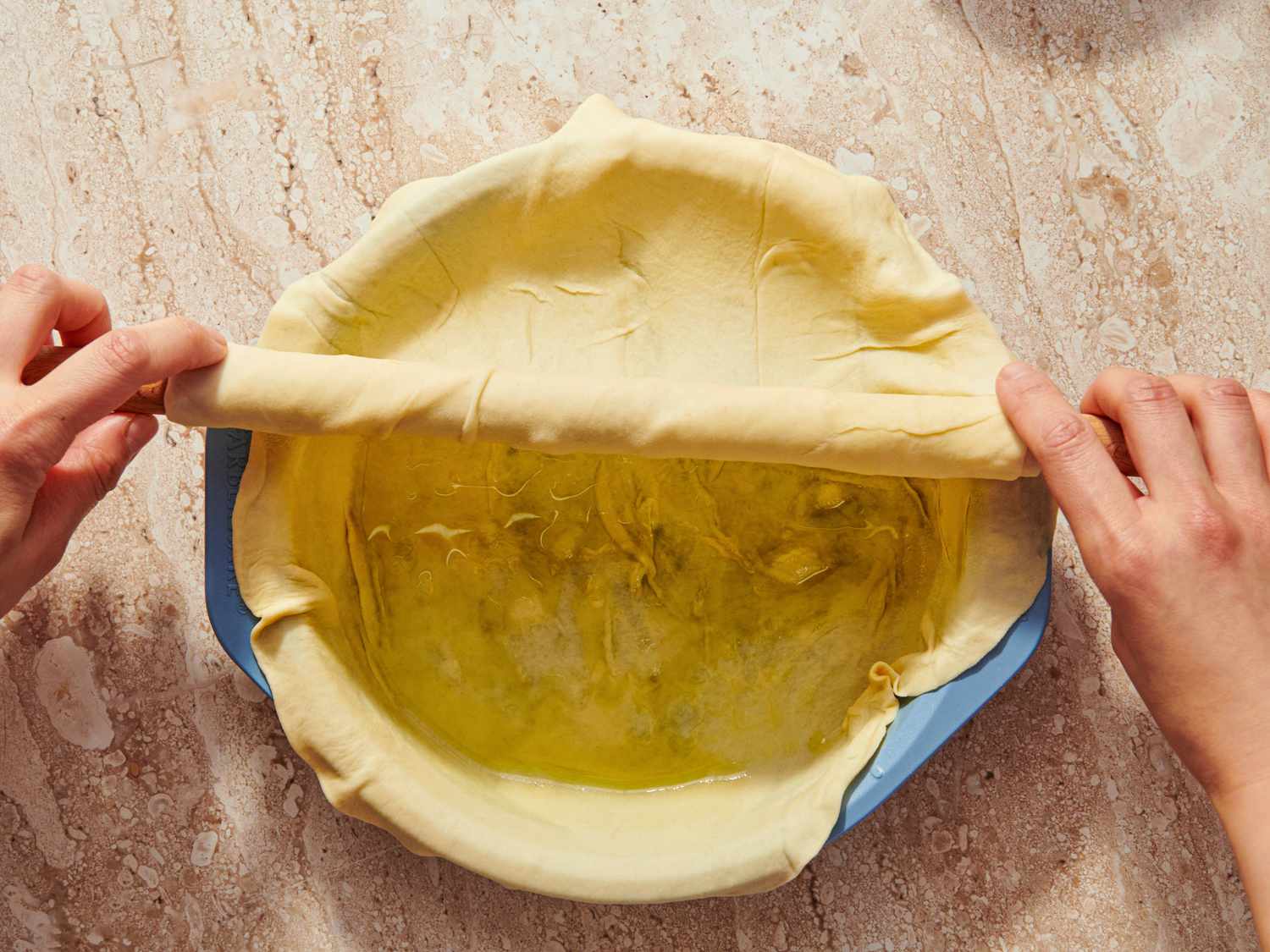 Hands folding phyllo dough over a dish on a marble surface