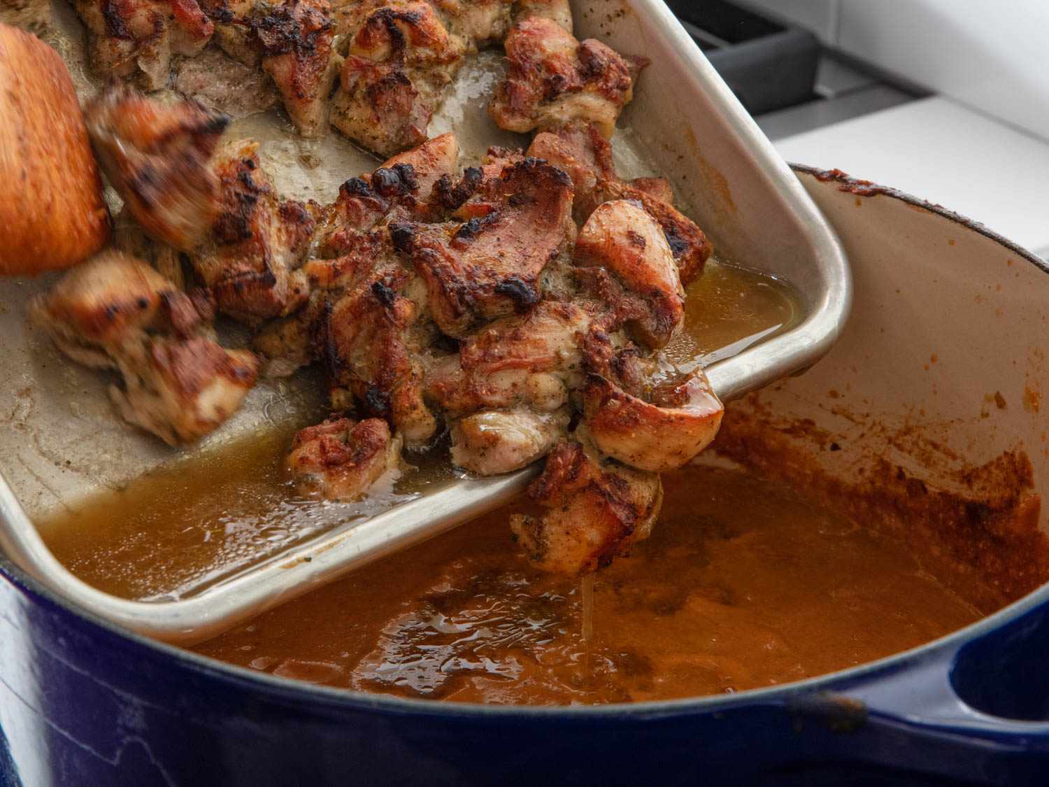 The broiled chicken and pan juices are scraped from the sheet pan and into the pot.