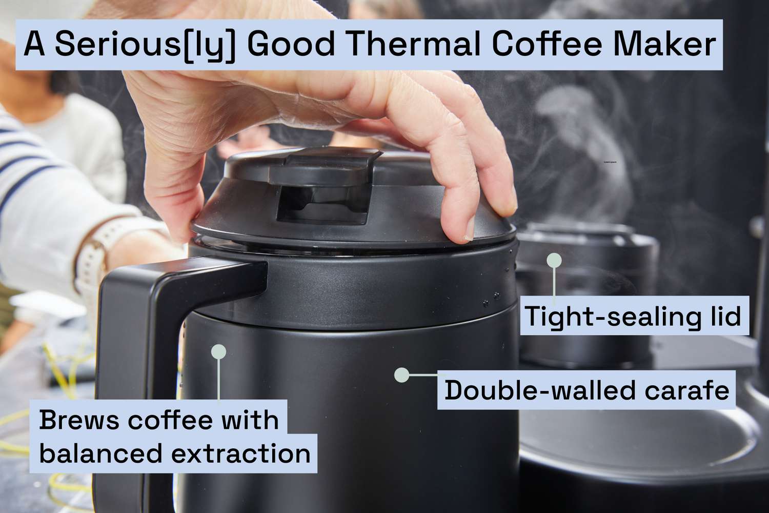 A person screwing the lid onto a thermal coffee carafe with steam wafting in the background