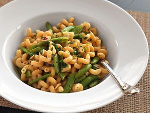 A wide white bowl containing a serving of pasta with snap peas, garlic, lemon zest, and black pepper.
