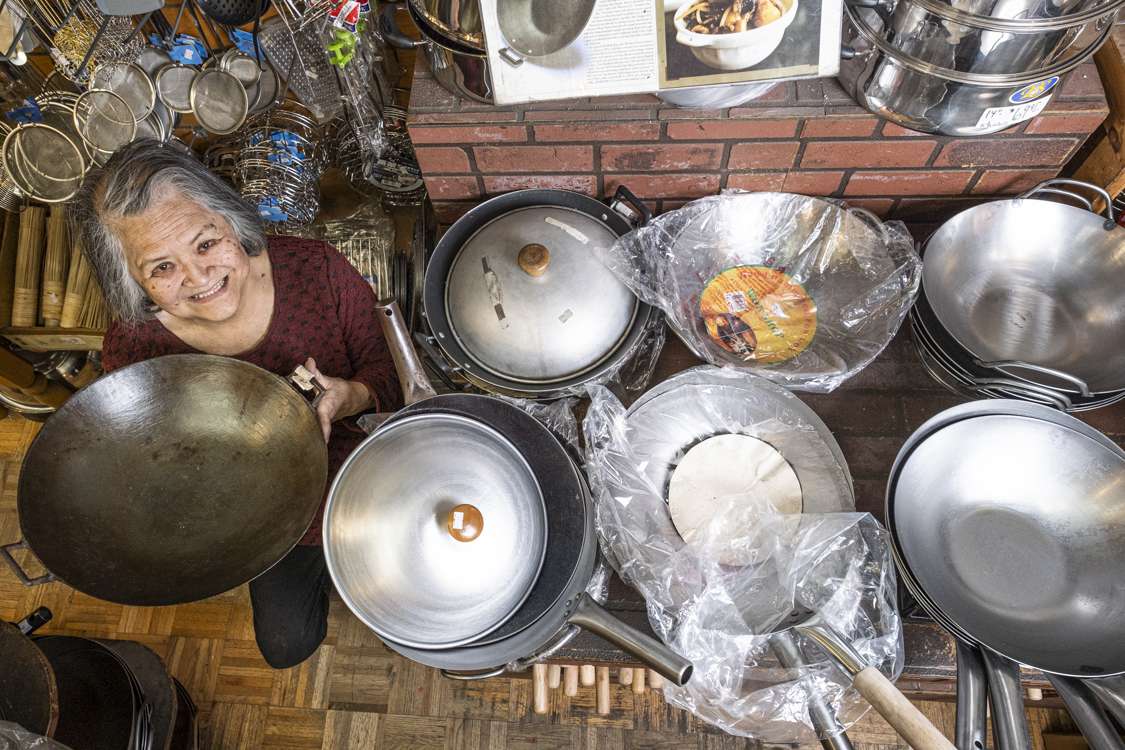 An overhead view of Tane Chan holding a wok next two 6 stacks of other woks