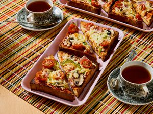 Slices of pizza toast arranged on a tray with cups of tea