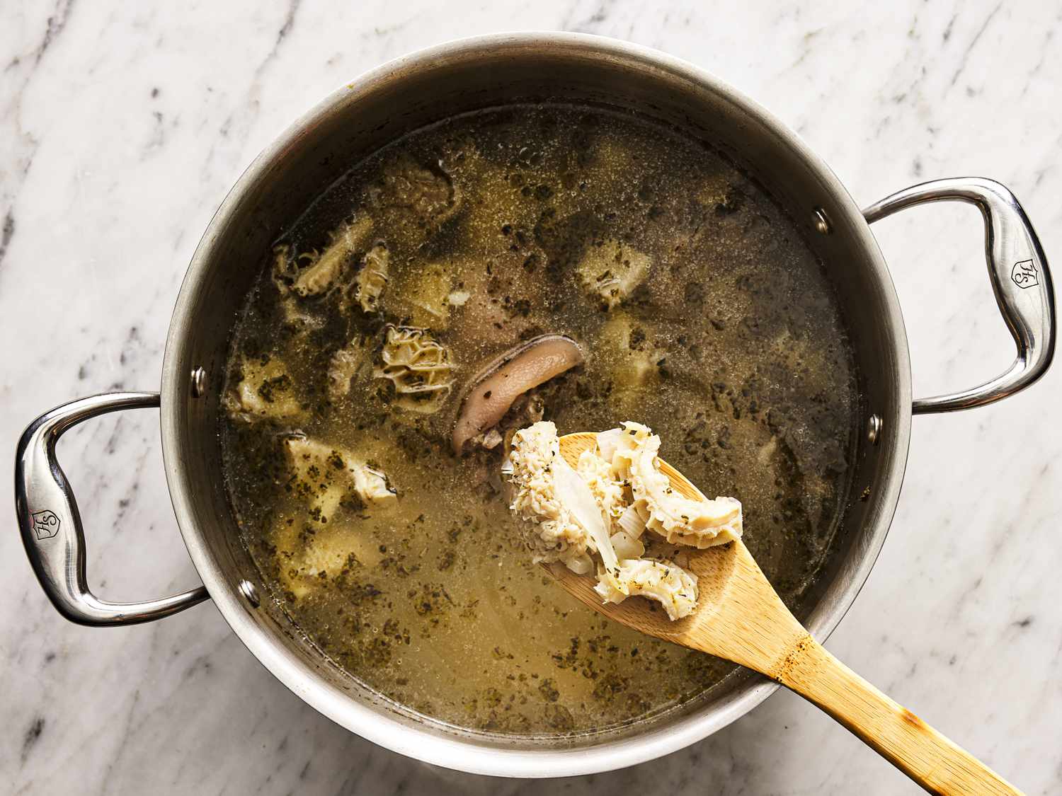 A wooden spoon lifting tripe up out of the stock pot.