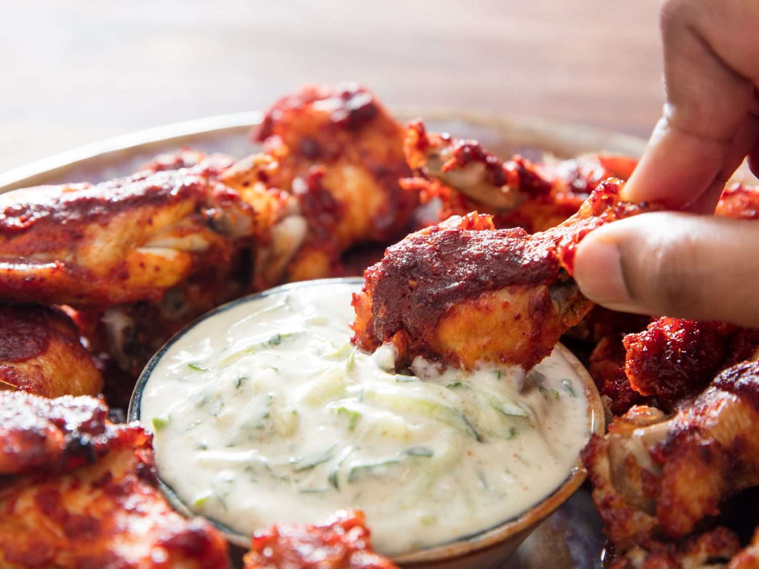 A chicken wing being dipped into a bowl of raitha.