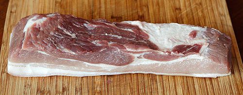 A lean slab of pork belly sitting on a cutting board.